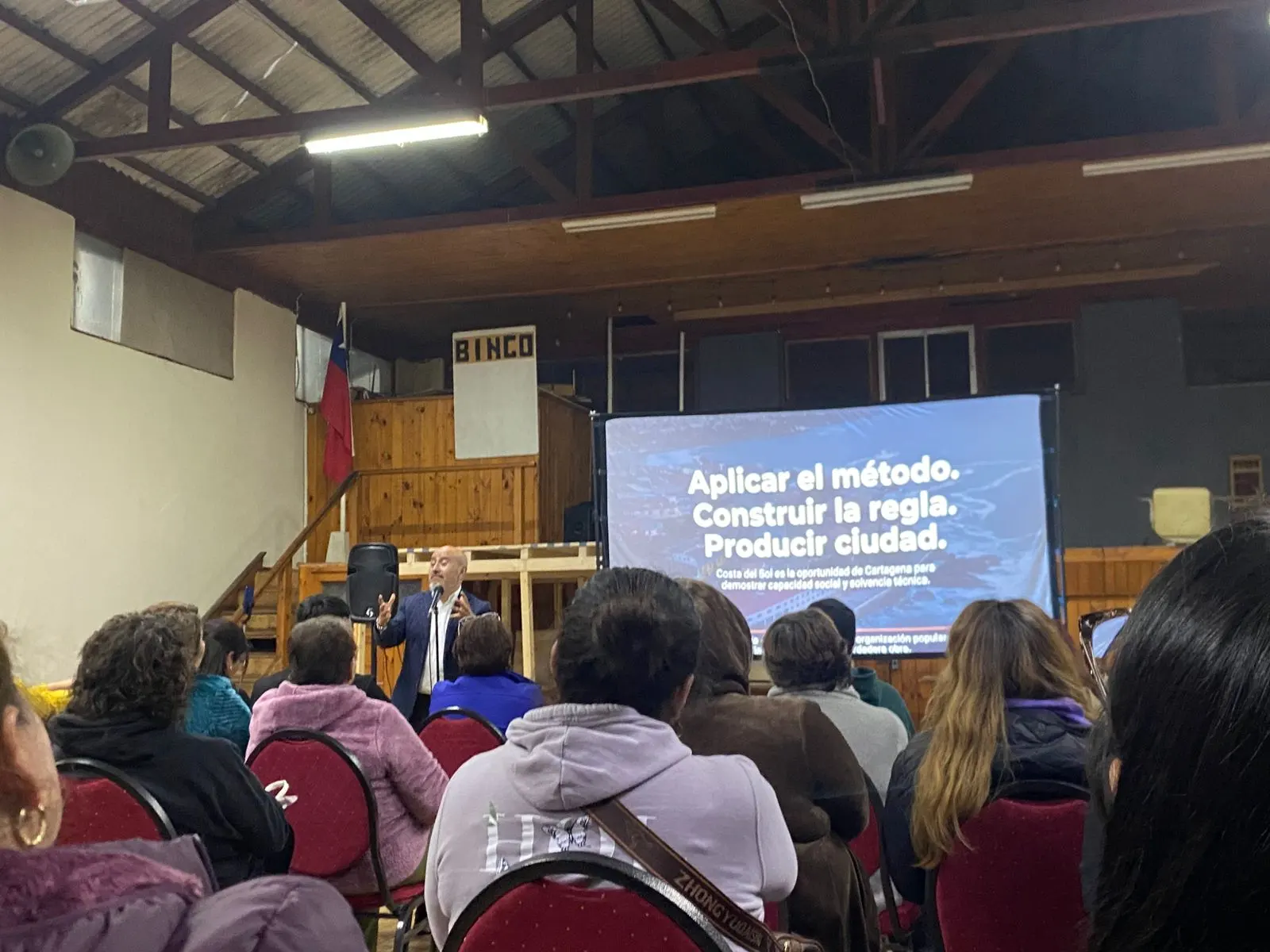 Ponente presentando ante el público con la pantalla del documental al fondo